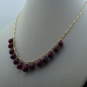 May include: A gold chain necklace with a row of teardrop-shaped red gemstones.