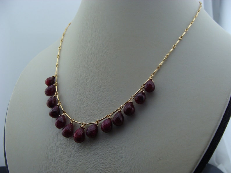 May include: A gold chain necklace with a row of teardrop-shaped red gemstones.