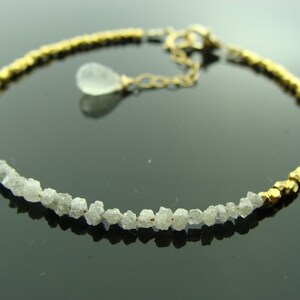May include: A gold and white bracelet with a row of rough diamonds and a gold chain with a clear teardrop pendant.