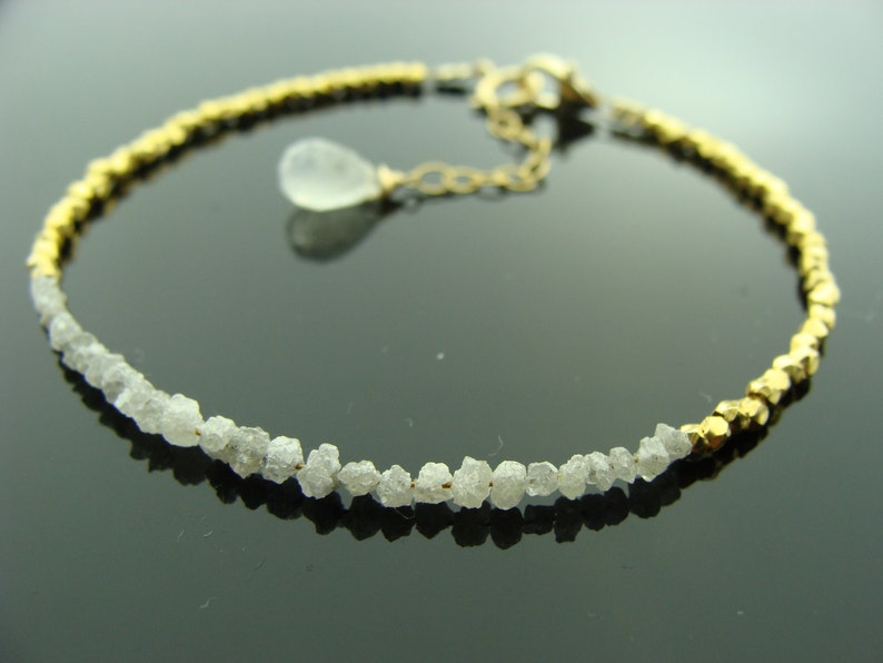 May include: A gold and white bracelet with a row of rough diamonds and a gold chain with a clear teardrop pendant.