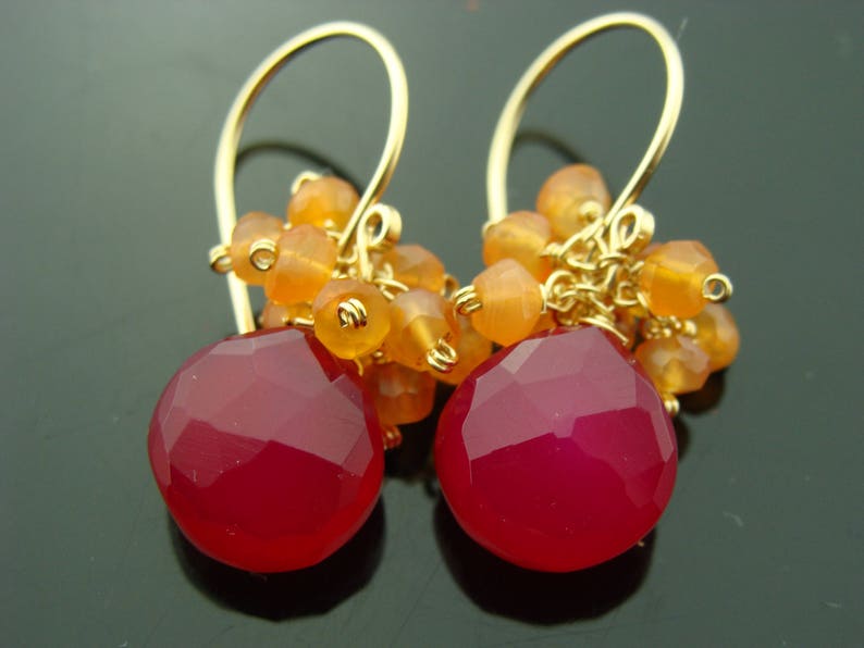 May include: Gold earrings with a cluster of orange carnelian beads and a large, faceted, pink chalcedony gemstone.