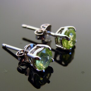 May include: A pair of silver earrings with green gemstone studs. The earrings have a post and butterfly back closure.