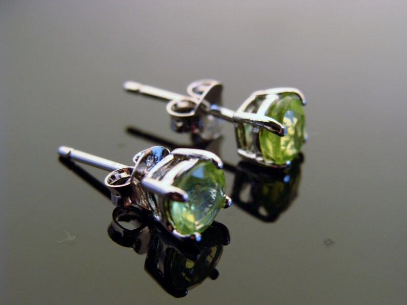 May include: A pair of silver earrings with green gemstone studs. The earrings have a post and butterfly back closure.