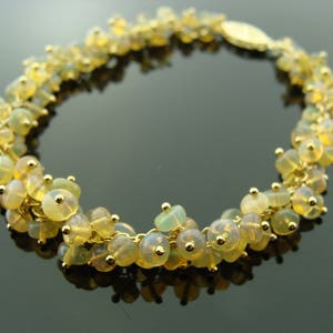 May include: A gold-toned bracelet featuring clusters of small, round, yellow-green beads. The beads are strung together with gold-colored links, and the bracelet has a gold clasp. The beads have a translucent quality, and the bracelet is displayed on a dark surface.
