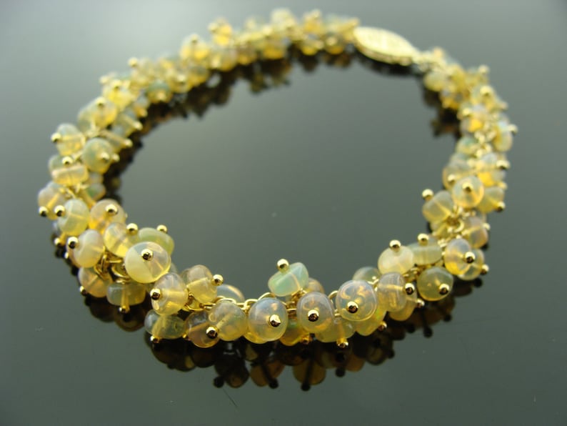 May include: A gold-toned bracelet featuring clusters of small, round, yellow-green beads. The beads are strung together with gold-colored links, and the bracelet has a gold clasp. The beads have a translucent quality, and the bracelet is displayed on a dark surface.
