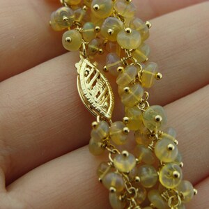 May include: Close-up of a gold-colored necklace with multiple strands of small, yellow-toned beads. The necklace features a decorative clasp and delicate gold chain links. The beads have a translucent quality, and the overall design is intricate.