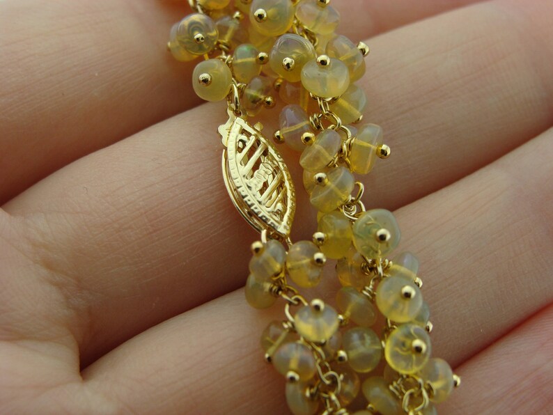 May include: Close-up of a gold-colored necklace with multiple strands of small, yellow-toned beads. The necklace features a decorative clasp and delicate gold chain links. The beads have a translucent quality, and the overall design is intricate.