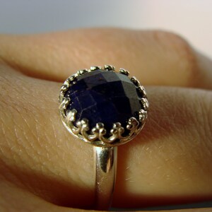 May include: A silver ring with a dark blue gemstone set in a decorative, ornate setting.