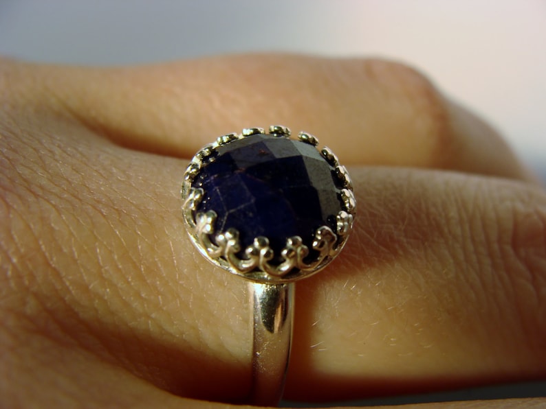 May include: A silver ring with a dark blue gemstone set in a decorative, ornate setting.