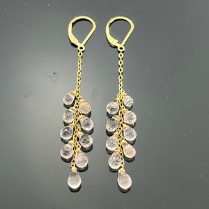 Pu&ograve; includere: Un paio di orecchini pendenti in oro con una catena e pi&ugrave; cristalli trasparenti rosa a forma di goccia.