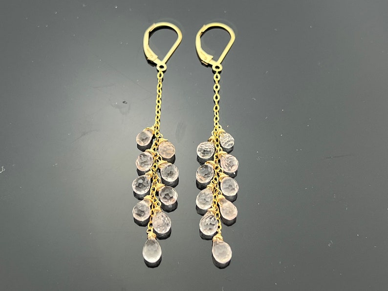 Pu&ograve; includere: Un paio di orecchini pendenti in oro con una catena e pi&ugrave; cristalli trasparenti rosa a forma di goccia.