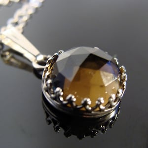 May include: A silver necklace featuring a faceted, round, brown gemstone pendant. The pendant is set in a decorative silver bezel. The chain is delicate and silver, creating a classic and elegant look.