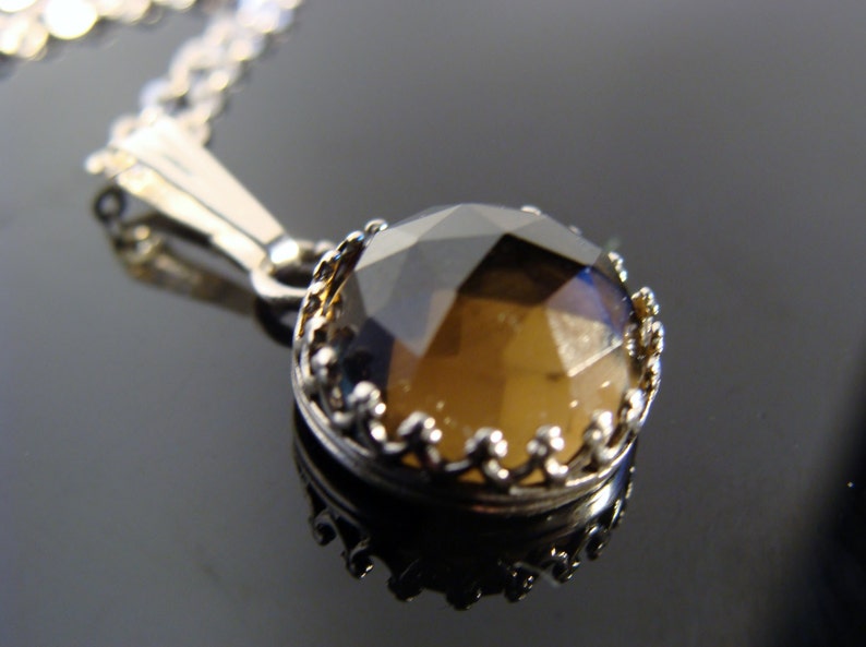 May include: A silver necklace featuring a faceted, round, brown gemstone pendant. The pendant is set in a decorative silver bezel. The chain is delicate and silver, creating a classic and elegant look.