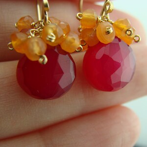 May include: A pair of earrings with a pink gemstone and orange carnelian beads. The earrings are made with gold wire and have a delicate, bohemian style.