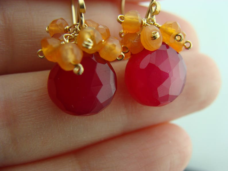 May include: A pair of earrings with a pink gemstone and orange carnelian beads. The earrings are made with gold wire and have a delicate, bohemian style.