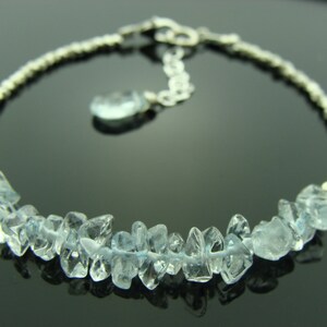 May include: A silver chain bracelet with a cluster of light blue aquamarine gemstones. The bracelet has a lobster clasp closure.