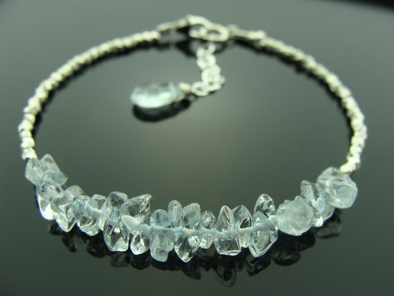May include: A silver chain bracelet with a cluster of light blue aquamarine gemstones. The bracelet has a lobster clasp closure.