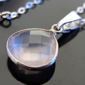 May include: A silver chain necklace with a teardrop-shaped pendant featuring a clear, faceted rose quartz stone.