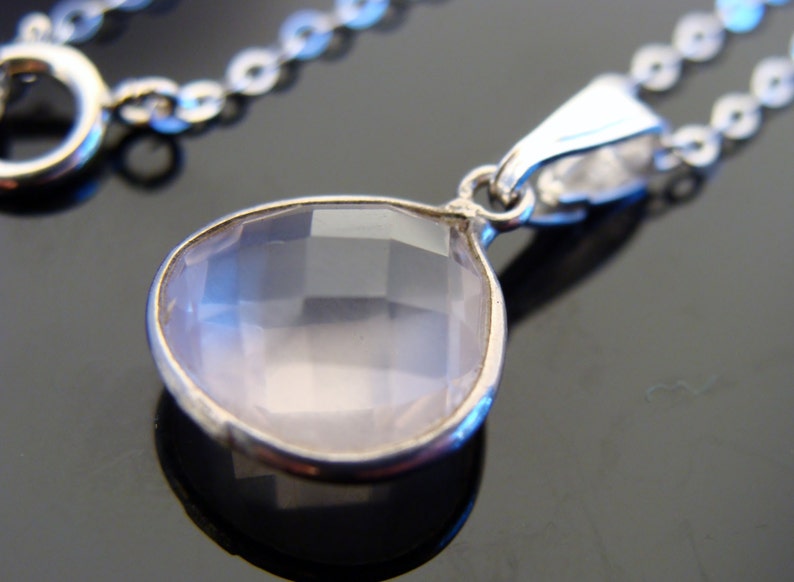 May include: A silver chain necklace with a teardrop-shaped pendant featuring a clear, faceted rose quartz stone.