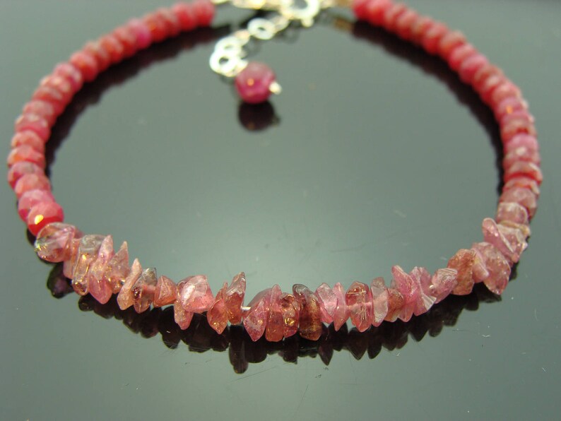 May include: A pink gemstone bracelet with a silver clasp. The bracelet is made of small, irregular shaped pink gemstones.