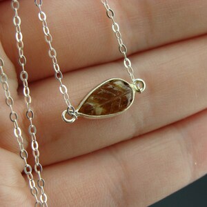 May include: A silver chain necklace with a teardrop-shaped pendant featuring a brown and gold leaf design.