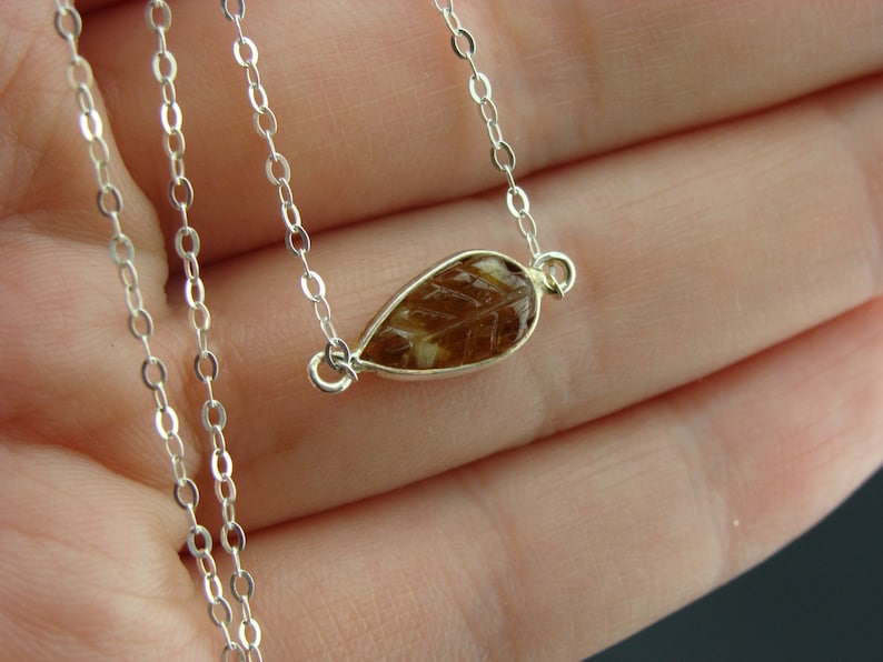 May include: A silver chain necklace with a teardrop-shaped pendant featuring a brown and gold leaf design.