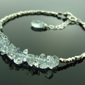 May include: A silver bracelet with a delicate chain and a row of light blue aquamarine stones. The stones are faceted and have a natural, irregular shape.