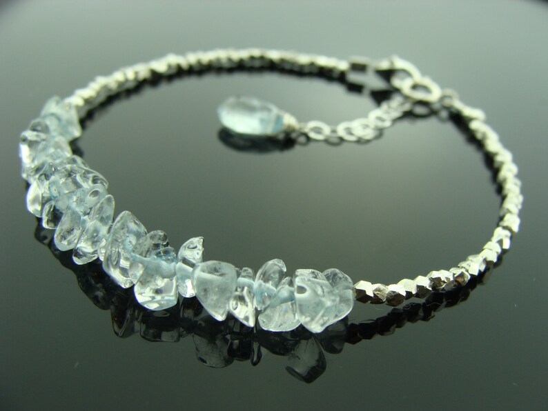 May include: A silver bracelet with a delicate chain and a row of light blue aquamarine stones. The stones are faceted and have a natural, irregular shape.