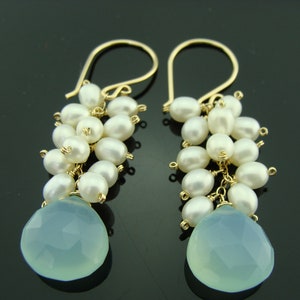 May include: Gold dangle earrings with a teardrop shaped light blue gemstone and a cluster of white pearls.
