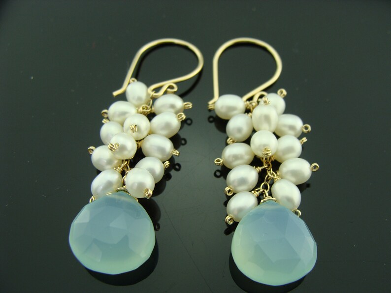 May include: Gold dangle earrings with a teardrop shaped light blue gemstone and a cluster of white pearls.