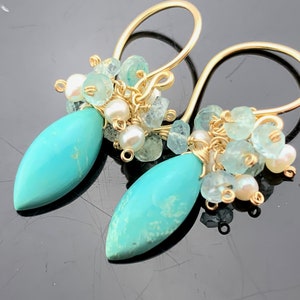Op de afbeelding: Gouden oorbellen met turquoise en aquamarijn stenen. De oorbellen hebben een traanvormige turquoise steen en een cluster van aquamarijn en witte parels.