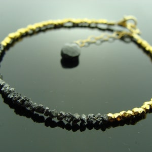 May include: A black diamond bracelet with gold beads. The bracelet is made of small, rough black diamonds and gold beads. The bracelet has a clasp closure.