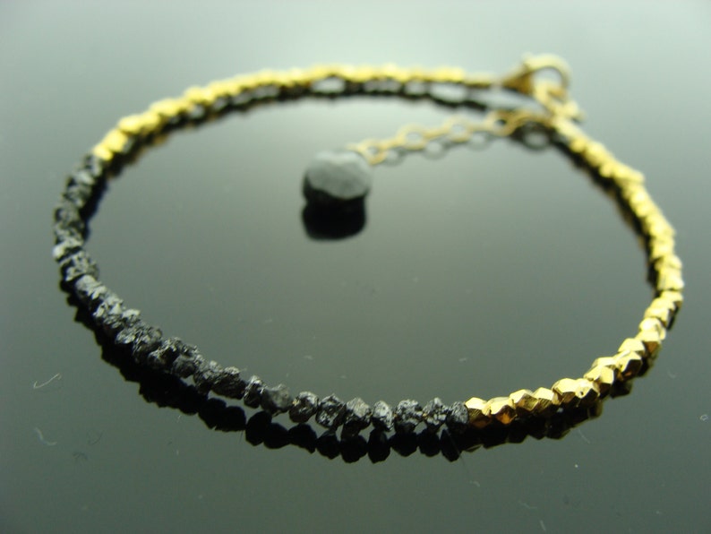 May include: A black diamond bracelet with gold beads. The bracelet is made of small, rough black diamonds and gold beads. The bracelet has a clasp closure.