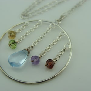 May include: A silver necklace with a circular pendant featuring five dangling gemstones: light blue, purple, green, and two shades of green. The pendant is suspended from a silver chain.