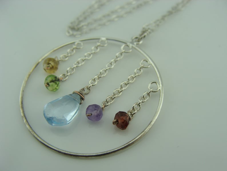 May include: A silver necklace with a circular pendant featuring five dangling gemstones: light blue, purple, green, and two shades of green. The pendant is suspended from a silver chain.