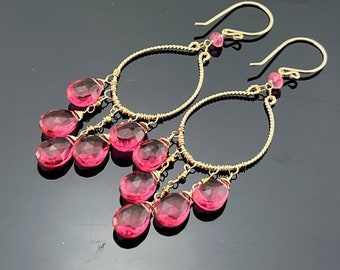 Puede incluir: Aretes de aro de oro con gotas de piedras preciosas rosas. Los aretes presentan un diseño delicado de alambre y varias piedras preciosas rosas que cuelgan de los aros.