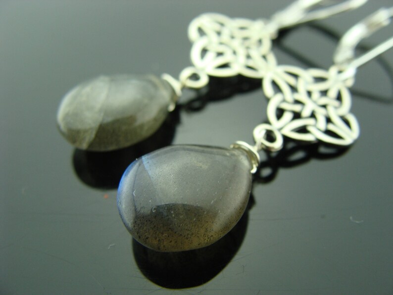 May include: Silver Celtic knot earrings with dark gray teardrop-shaped gemstone pendants.