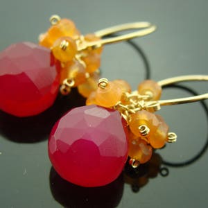 May include: A pair of gold earrings with pink and orange gemstone drops. The earrings feature a cluster of smaller orange gemstones and a larger pink gemstone drop.
