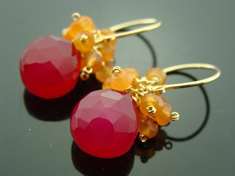 May include: A pair of gold earrings with pink and orange gemstone drops. The earrings feature a cluster of smaller orange gemstones and a larger pink gemstone drop.
