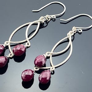 Peut inclure: Paire de boucles d'oreilles pendantes en argent avec trois pierres précieuses rouge foncé à facettes suspendues à une boucle décorative en argent. Fermeture à crochet simple.