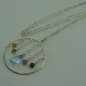 May include: A silver necklace with a circular pendant featuring a light blue gemstone and smaller gemstones in green, yellow, purple, and brown.