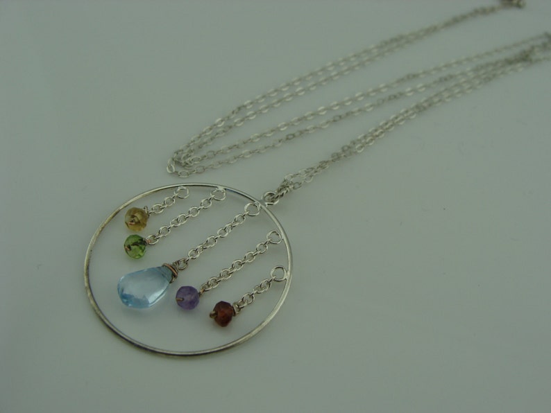 May include: A silver necklace with a circular pendant featuring a light blue gemstone and smaller gemstones in green, yellow, purple, and brown.