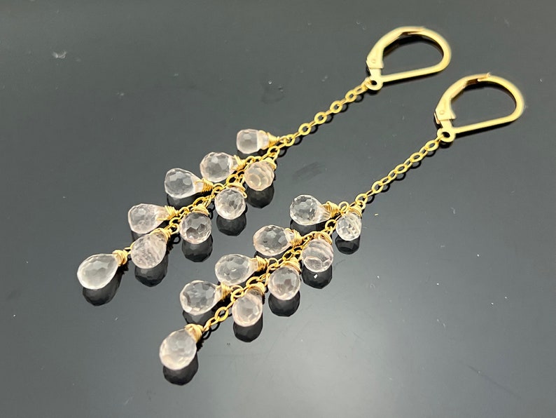 Pu&ograve; includere: Un paio di orecchini pendenti in oro con un design a cascata di pietre preziose rosa pallido a forma di lacrima.