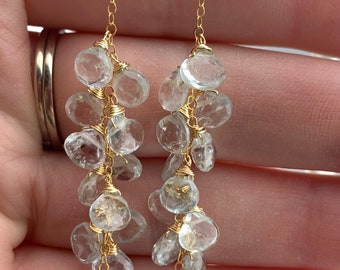 May include: Gold dangle earrings with a cluster of light blue aquamarine stones hanging from a delicate gold chain.