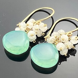 May include: Gold dangle earrings with a light green gemstone and a cluster of white stones.
