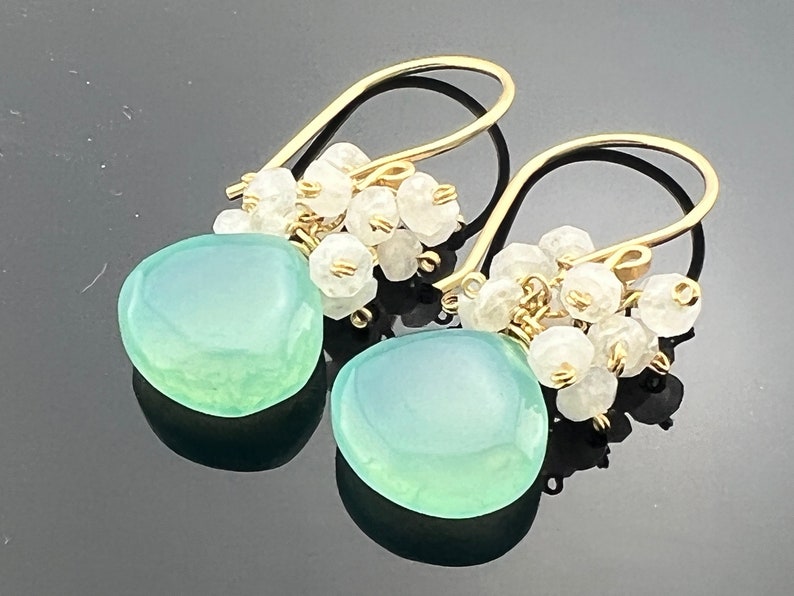 May include: Gold dangle earrings with a light green gemstone and a cluster of white stones.