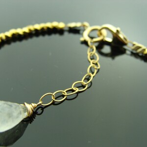 May include: A gold chain bracelet with a clear teardrop-shaped gemstone pendant. The bracelet has a lobster clasp closure.
