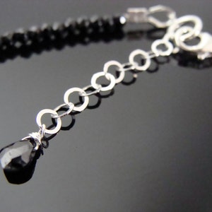 May include: A black onyx gemstone bracelet with a silver chain and clasp. The bracelet features a small black onyx gemstone dangle at the end of the chain.