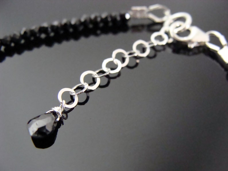May include: A black onyx gemstone bracelet with a silver chain and clasp. The bracelet features a small black onyx gemstone dangle at the end of the chain.