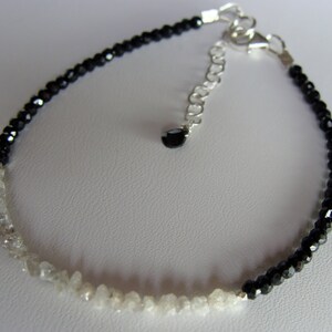 May include: A black and white beaded bracelet with a silver clasp. One half of the bracelet is made of black beads, and the other half is made of white beads.